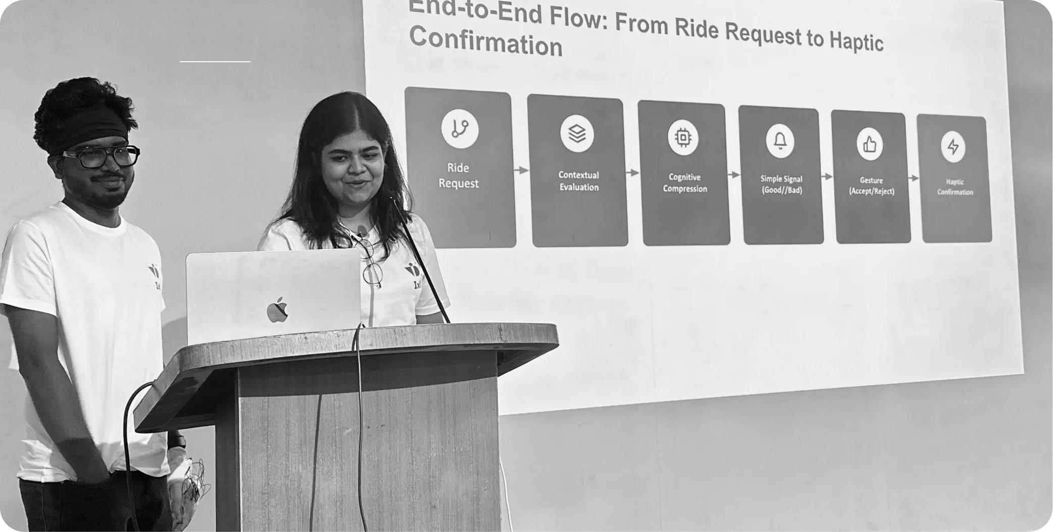 Akhil and Anjali at a lectern presenting Tapp at IxD Day, a slide behind them reading “End-to-End Flow: From Ride Request to Haptic Confirmation”