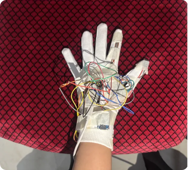 A white glove on a red cloth with sensors and wires taped along the fingers