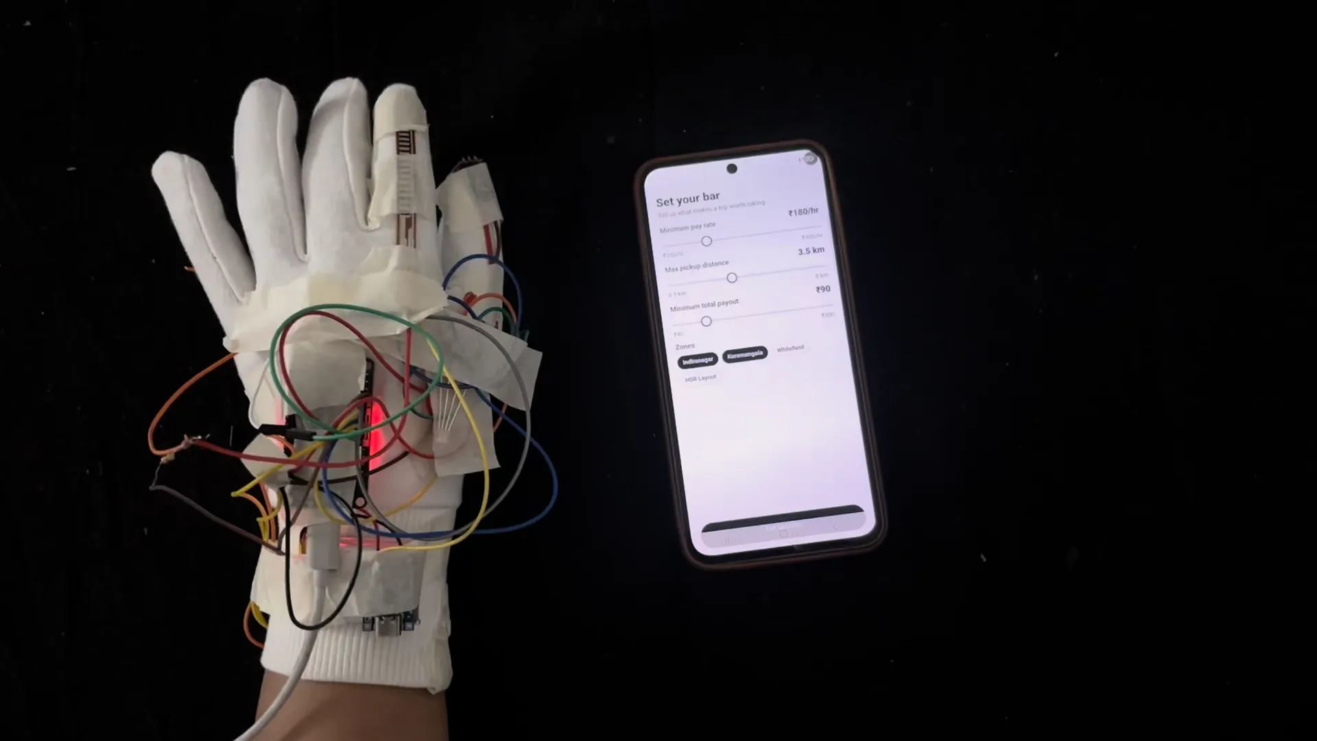 The wired glove glowing green next to a phone running the Tapp app on a black cloth